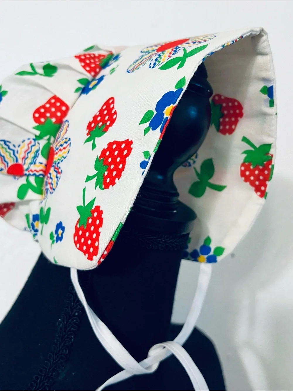 Charming vintage-style baby sunbonnet features a playful white fabric patterned